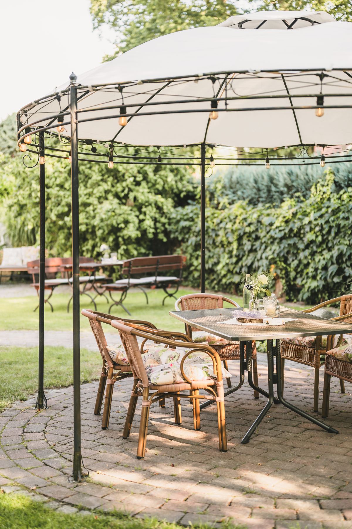 Gartenpavillon mit Rattanstühlen und gedecktem Tisch im Grünen