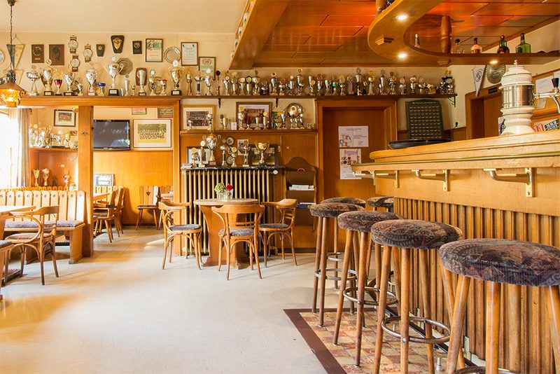 Kneipe mit Theke, Barhockern und Pokalen an der Wand