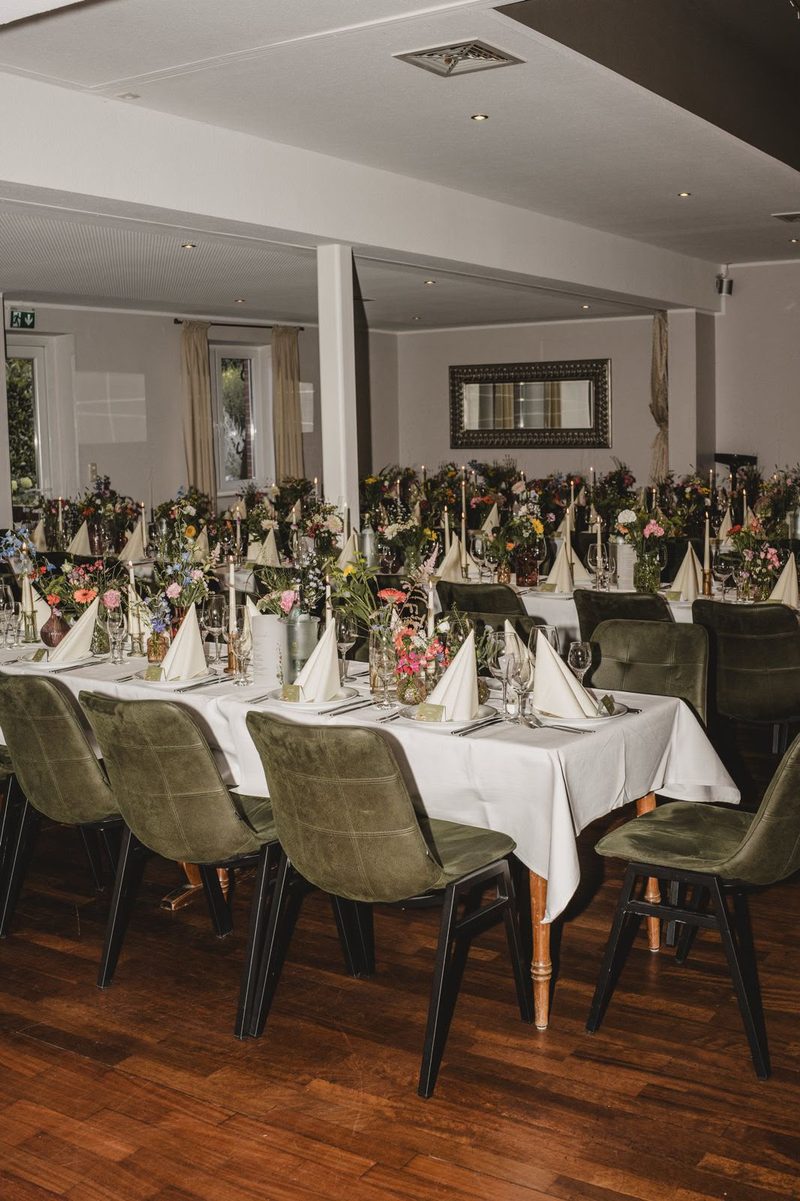 Lange weiß gedeckte Festtafel im Saal mit bunten Blumen und Kerzen